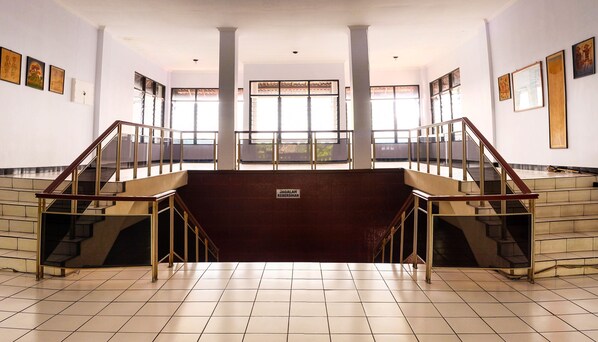 A spacious interior with a central staircase, large windows, and artwork on the walls. - Hotel Wisata (Magelang)
