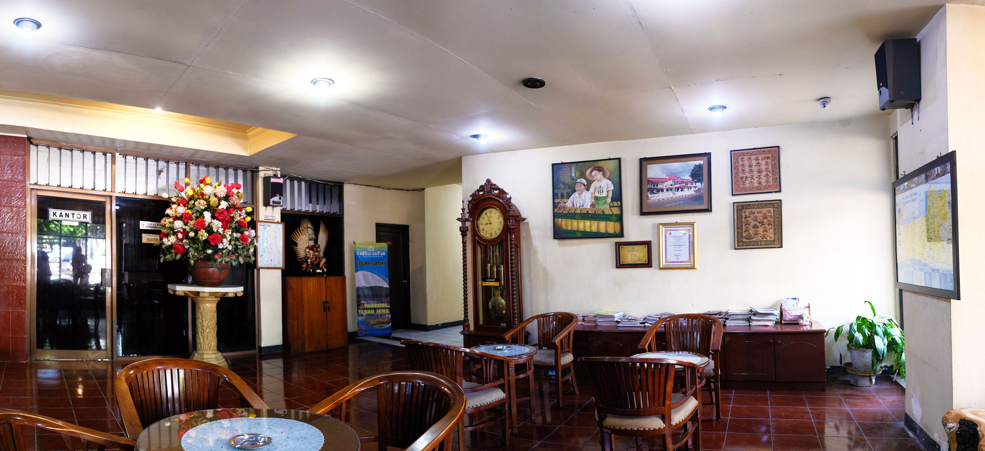 A hotel lobby with wooden chairs, a reception desk, a large clock, and several framed pictures on the walls.