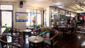 Interior de un restaurante con sillas y mesas de madera, un mapa en la pared y una tienda de ropa al fondo.