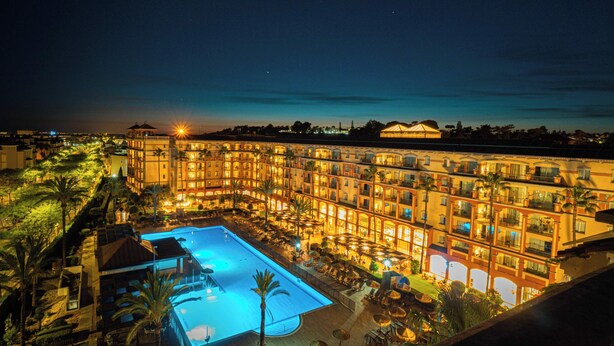 A hotel with multiple balconies, a swimming pool, and palm trees. - Ohtels Islantilla (Lepe)