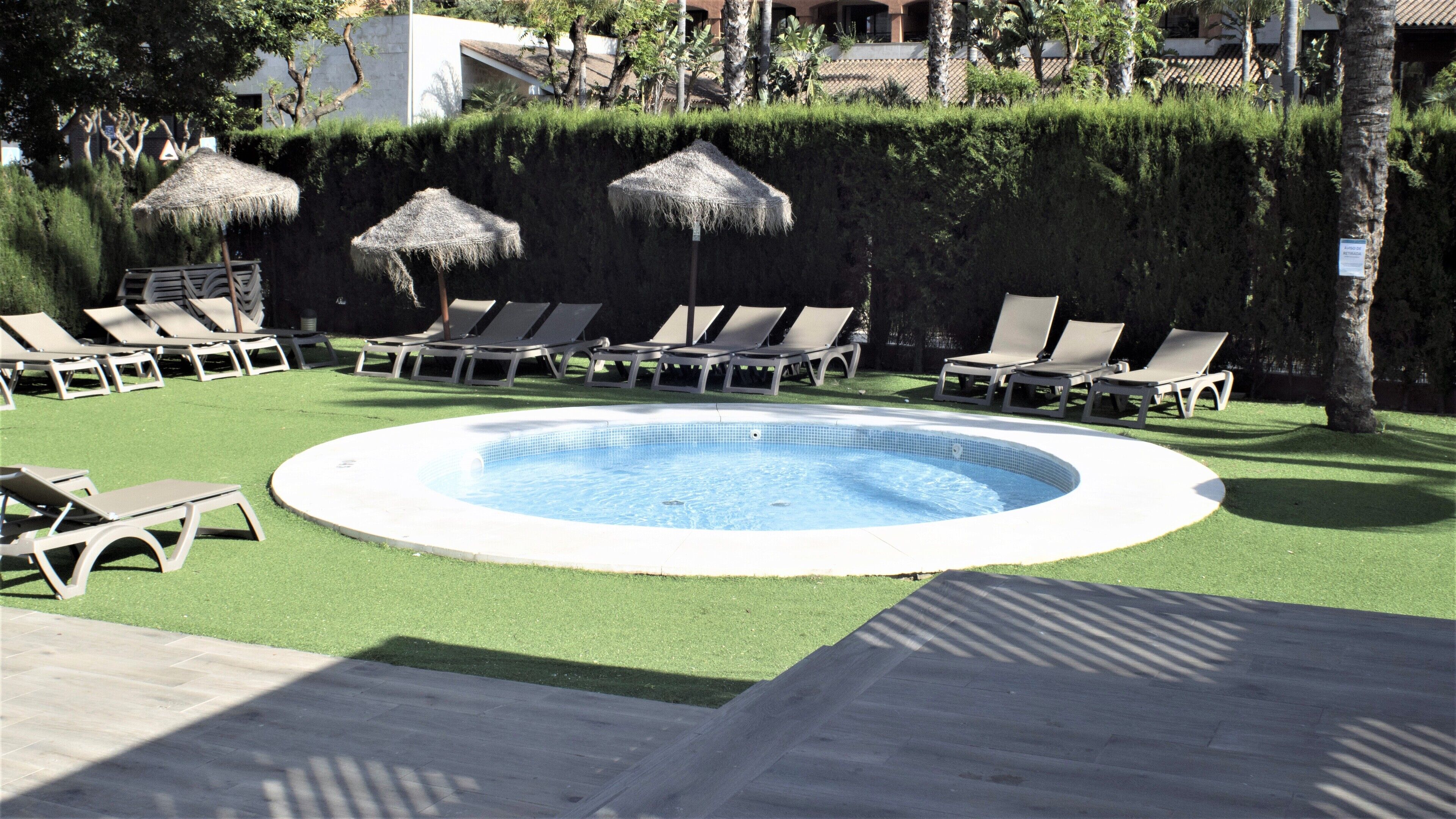 A circular pool with lounge chairs and thatched umbrellas around it.