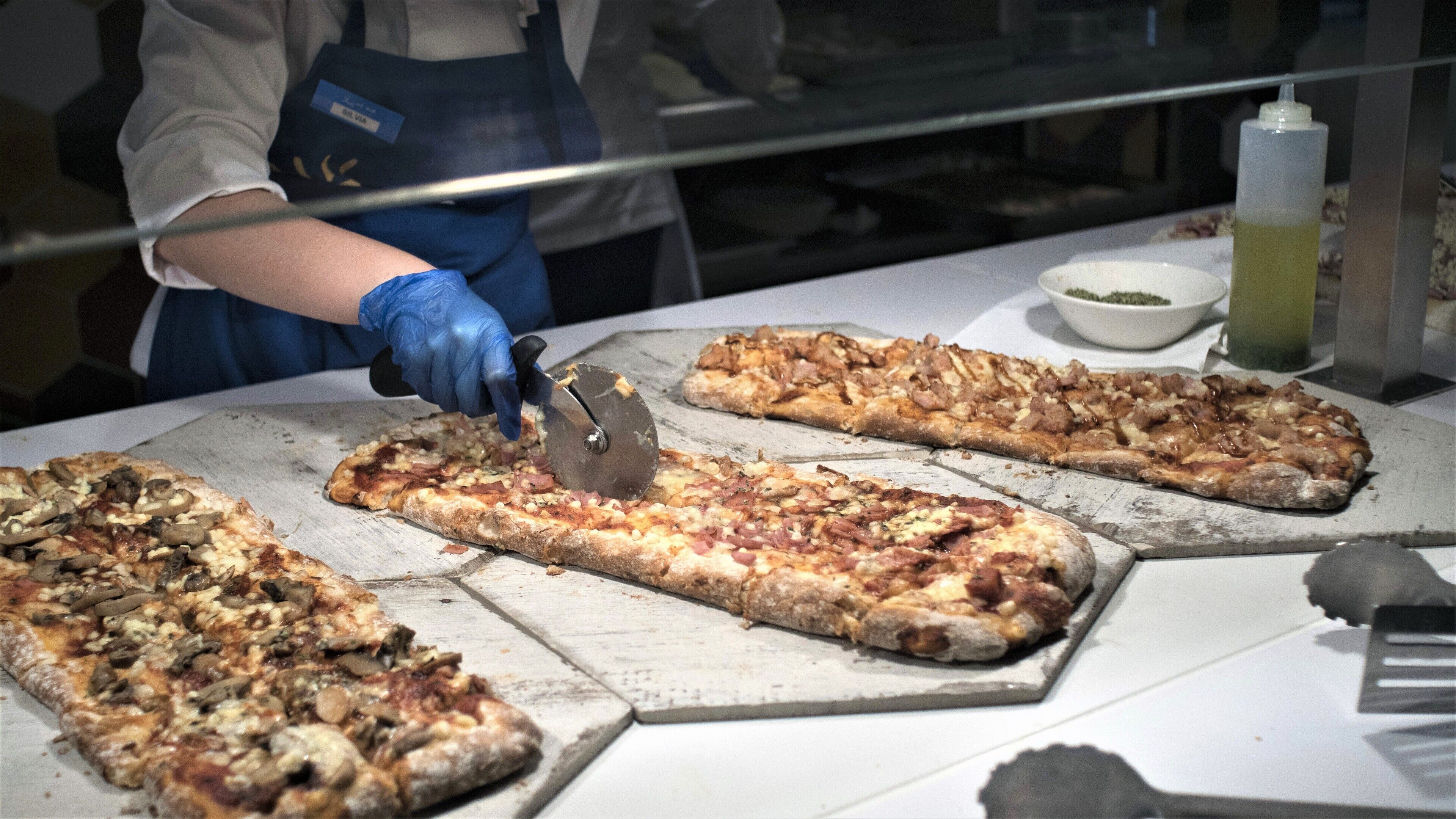A person cutting a large pizza on a wooden cutting board.