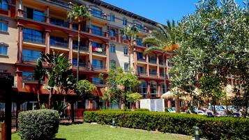 A multi-story hotel with balconies, a well-maintained lawn, and a parking area with several cars.