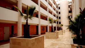 A multi-level atrium with a high ceiling, palm trees, and a checkered floor. - Ohtels Islantilla (Lepe)