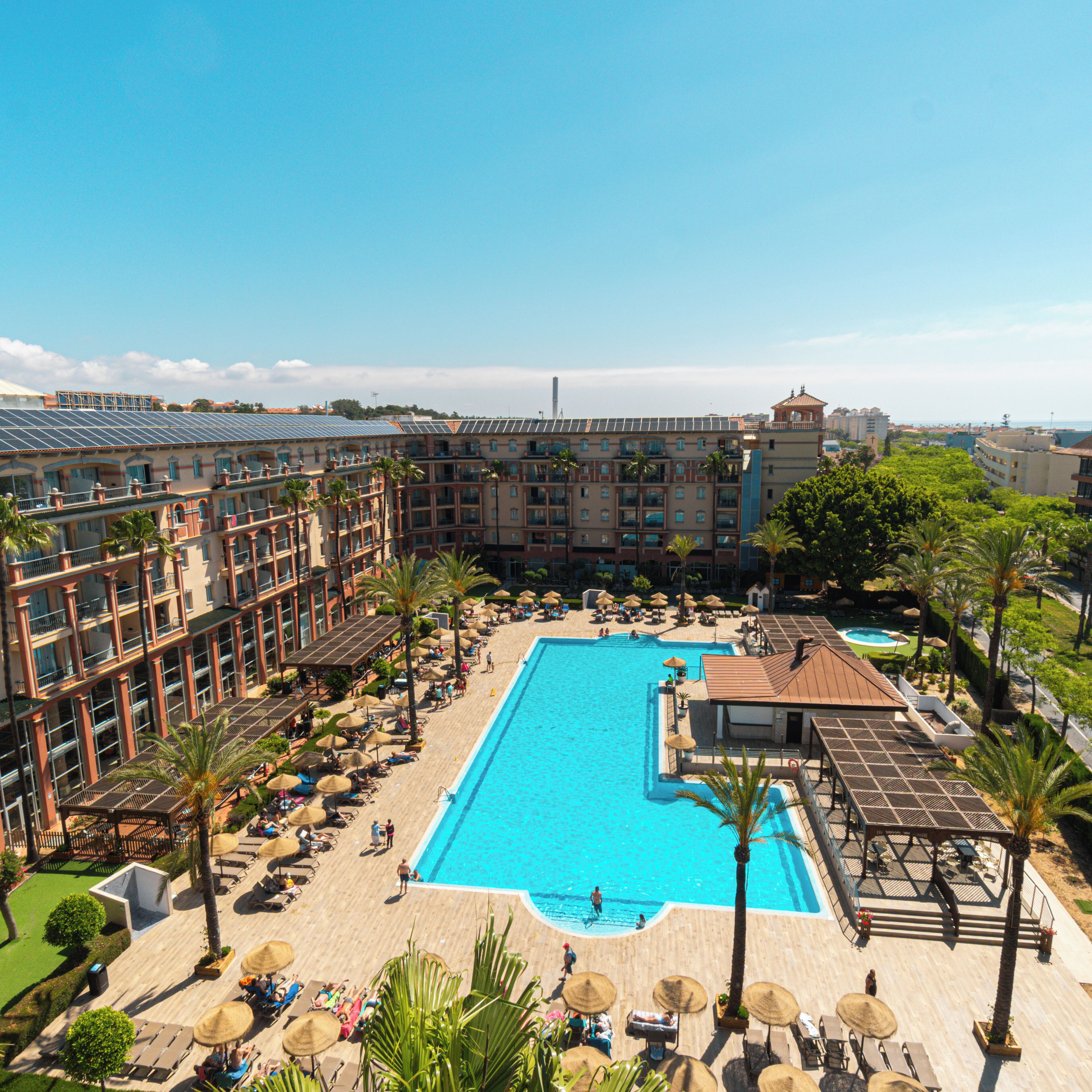 A resort with a large pool, sun loungers, umbrellas, and a view of the sea.
