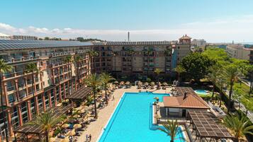 A resort with a large pool, sun loungers, umbrellas, and a view of the sea.