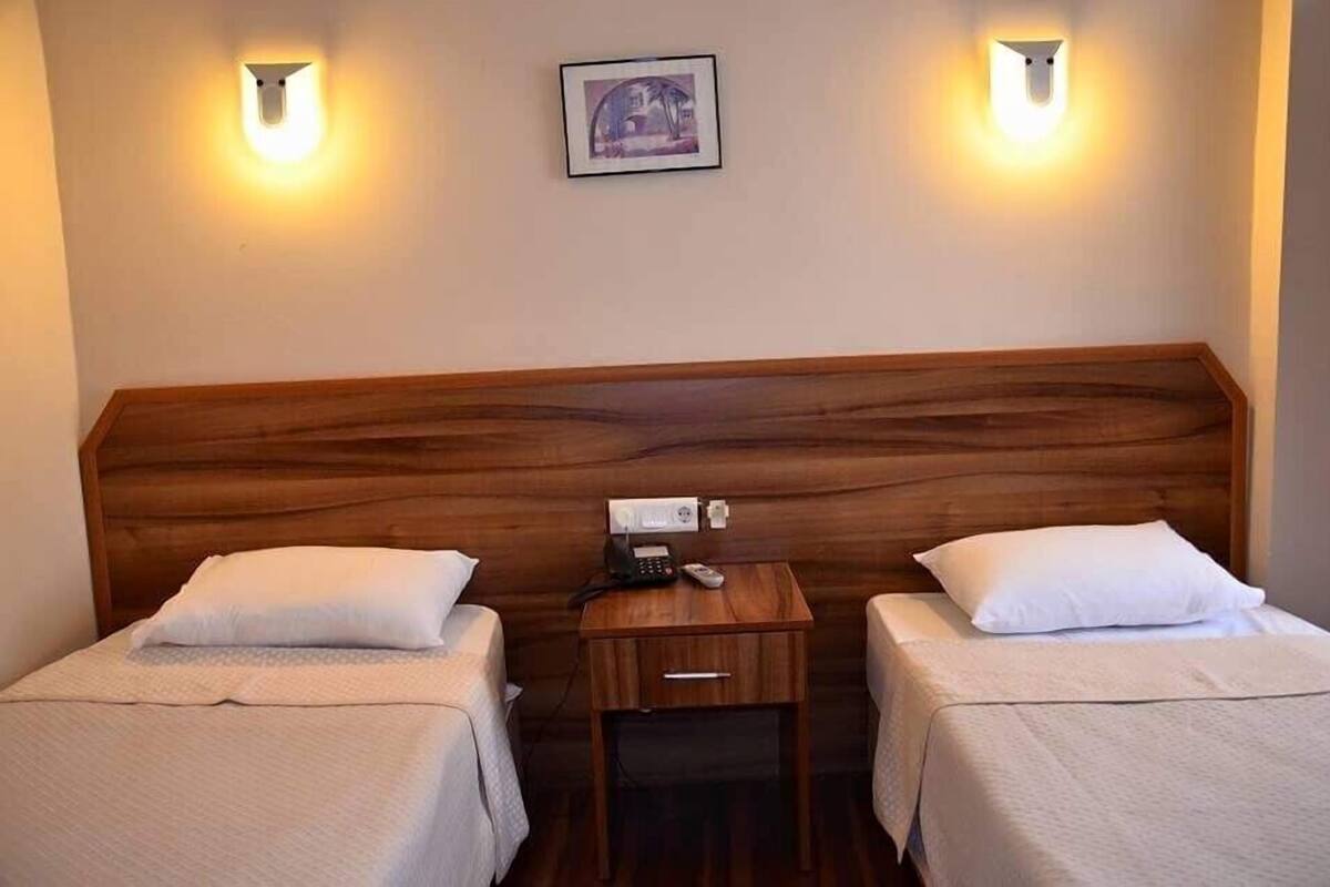 A hotel room with two single beds, a wooden headboard, bedside tables with lamps, and a framed picture on the wall.