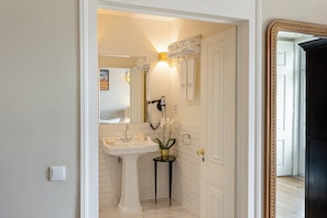 Un baño con lavamanos pedestal, un espejo y un perchero para toallas.