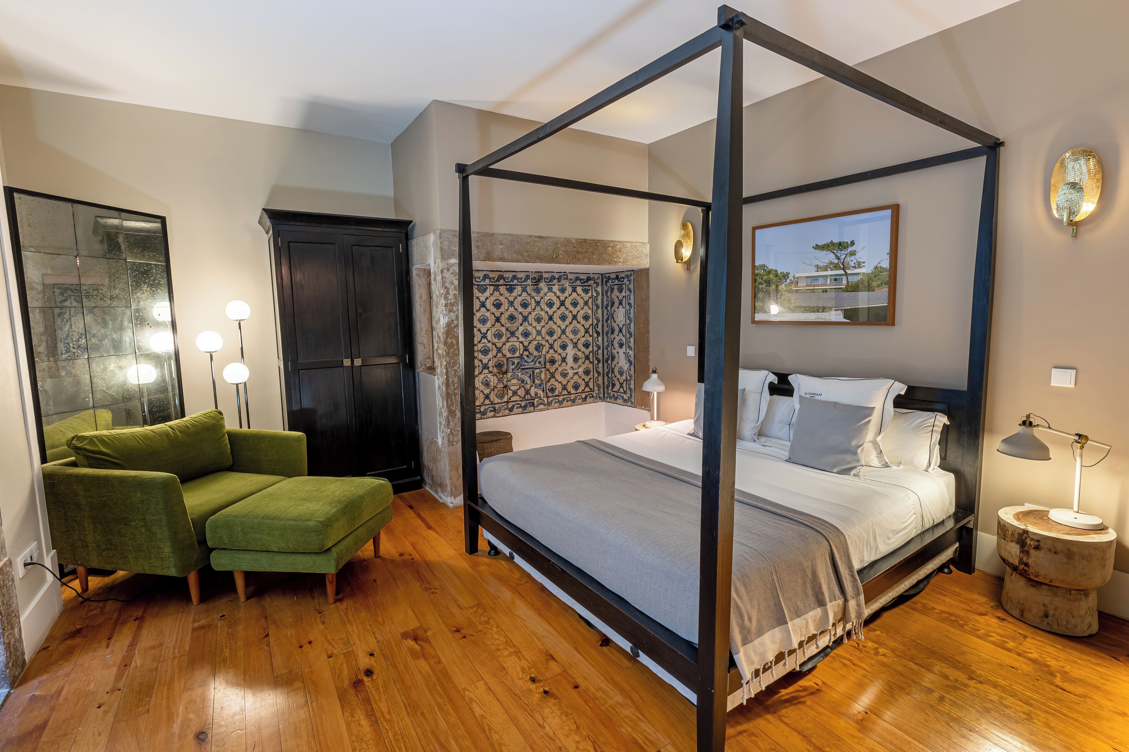 A bedroom with a four-poster bed, a green sofa, a wooden floor, and a patterned wall.