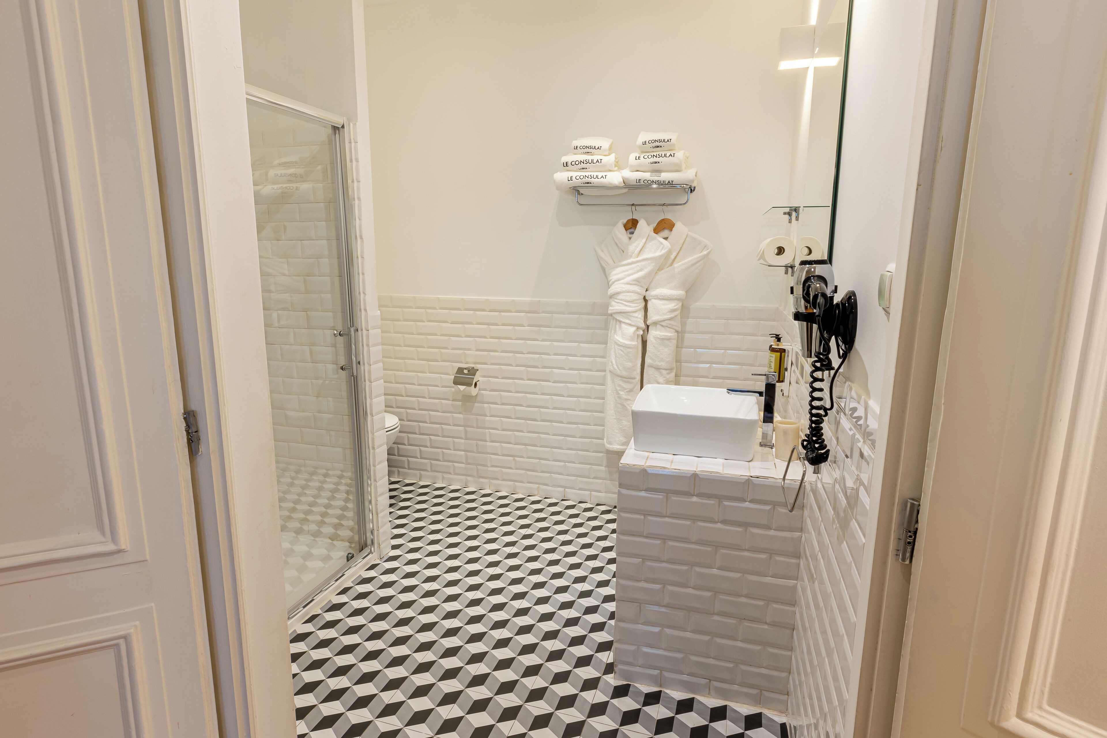 Een badkamer met een zwart-wit schakeerd motief vloer, een glazen douchecabine, toilet, wastafel en spiegel.