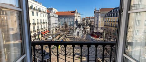 Vista desde una ventana sobre una plaza urbana con edificios históricos, un tranvía y una estatua.
