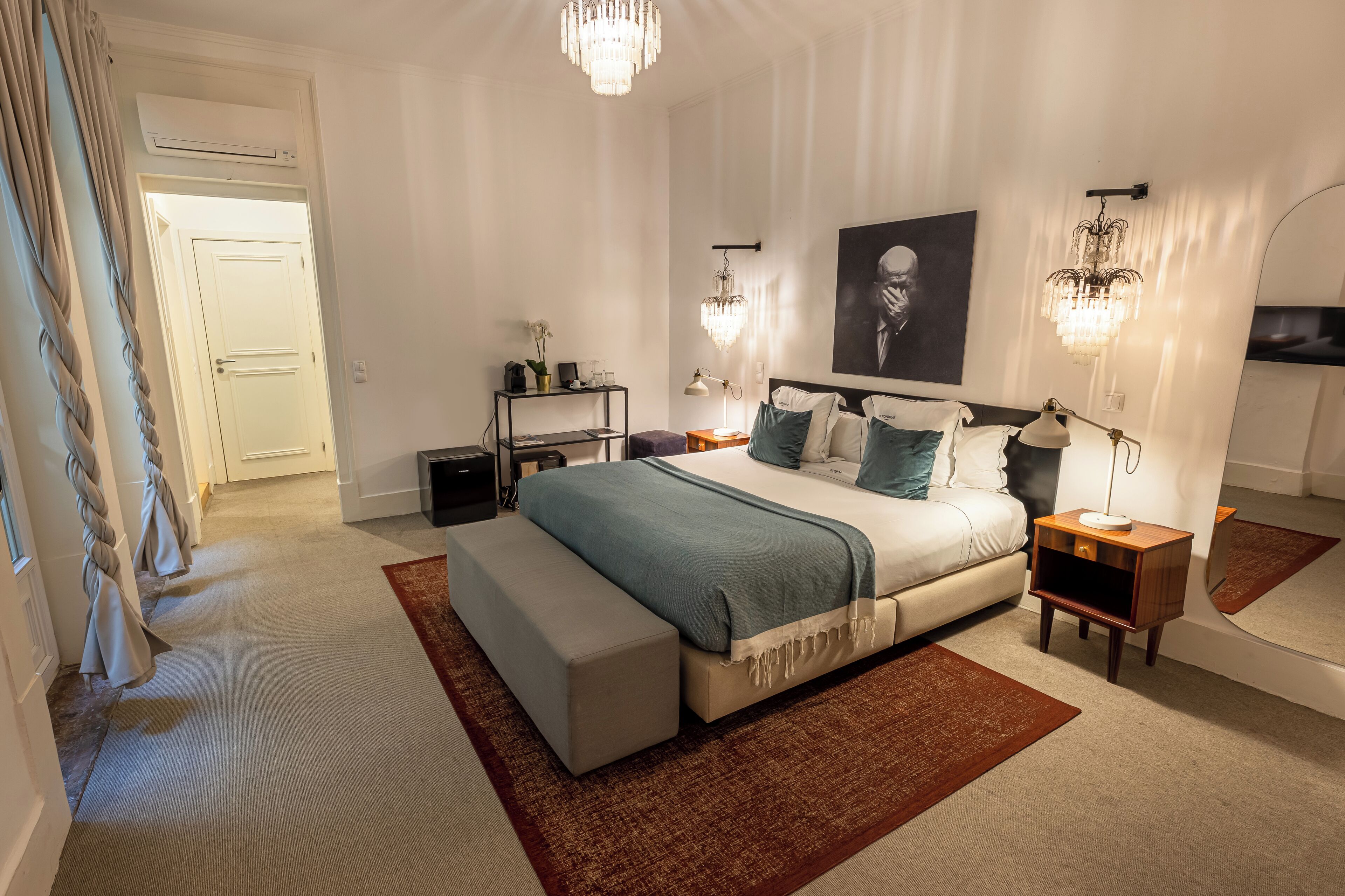 Un dormitorio moderno con una cama grande, mesitas de noche, un atril y una araña.