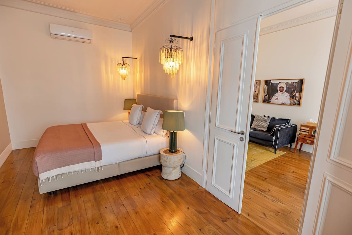 Un dormitorio con cama, lámparas de noche, aire acondicionado instalado en la pared y una puerta que da a otra habitación.