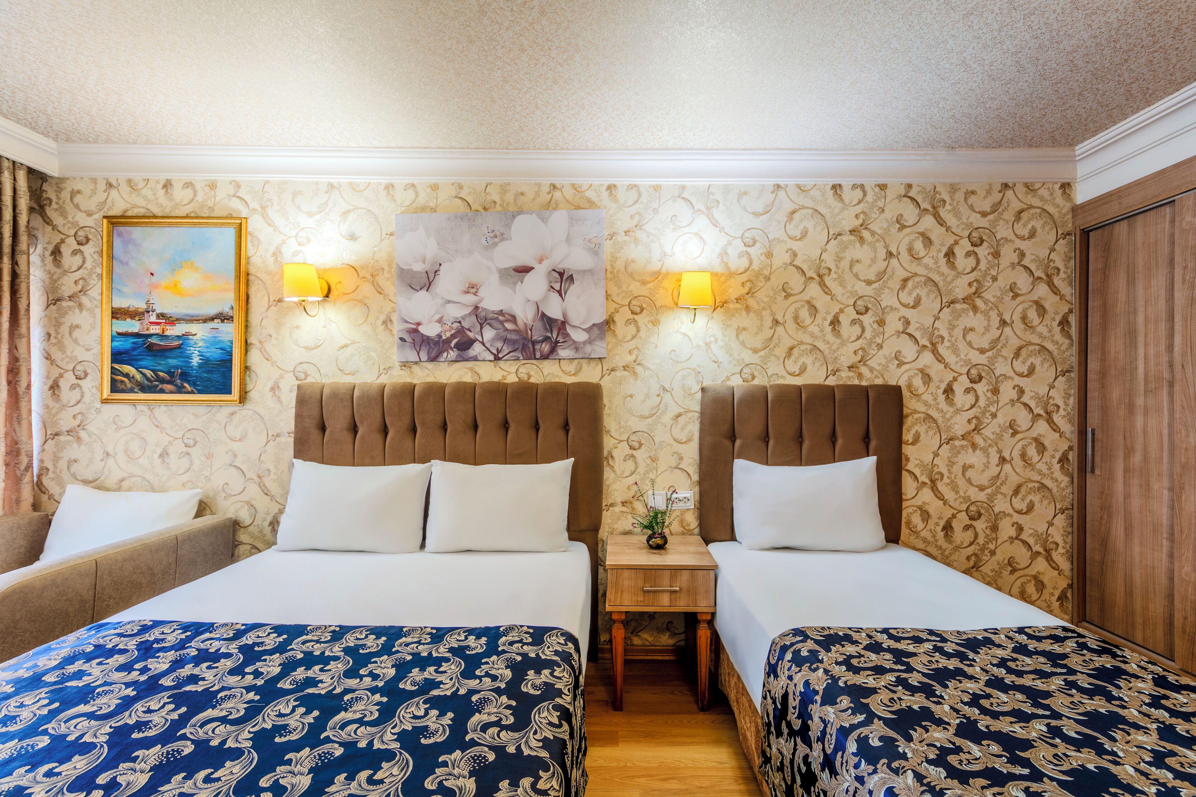 A hotel room with two beds, a nightstand, a lamp, and a painting on the wall.