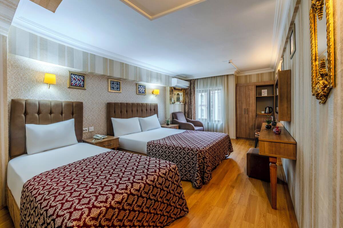 Habitación de hotel con dos camas, un escritorio, una silla, un televisor y un espejo.
