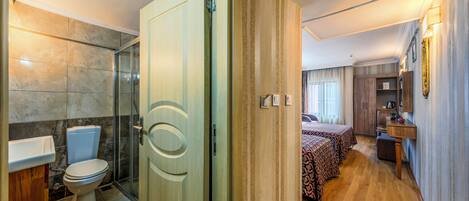 A hotel room with a bathroom, a shower, a bed, a desk, and a wardrobe.