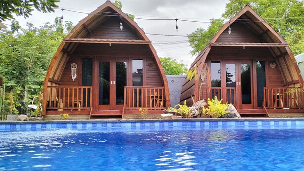 Two wooden cabins with balconies, a swimming pool, and lush greenery. - Pavilla Labuan Bajo (Labuan Bajo)