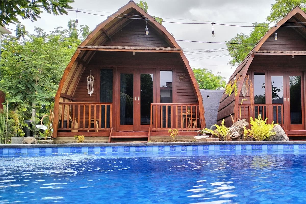 Two wooden cabins with balconies, a swimming pool, and lush greenery.