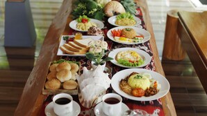 A long wooden table with various dishes and drinks, set in an outdoor area with bamboo plants and a view of the sea. - Pavilla Labuan Bajo (Labuan Bajo)