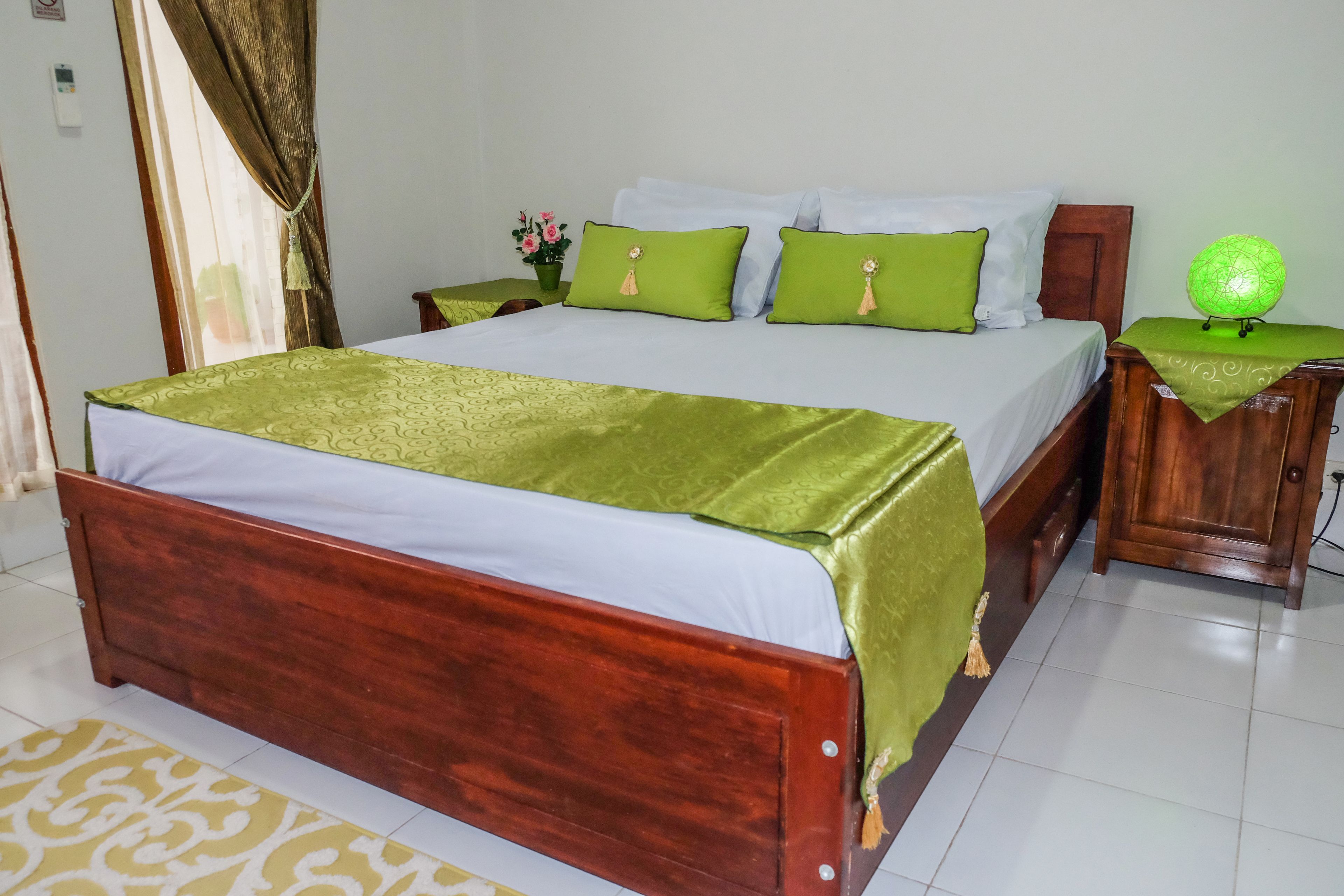 A neatly made bed with green and white bedding, a wooden headboard, and a bedside table with a green lamp.