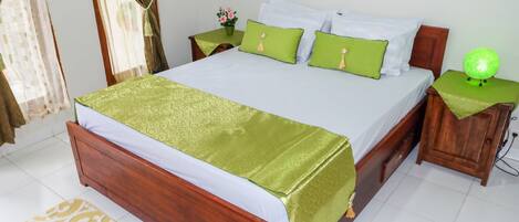 A neatly made bed with a green bedspread and pillows, a bedside table with a green lamp, and a small potted plant on the nightstand.
