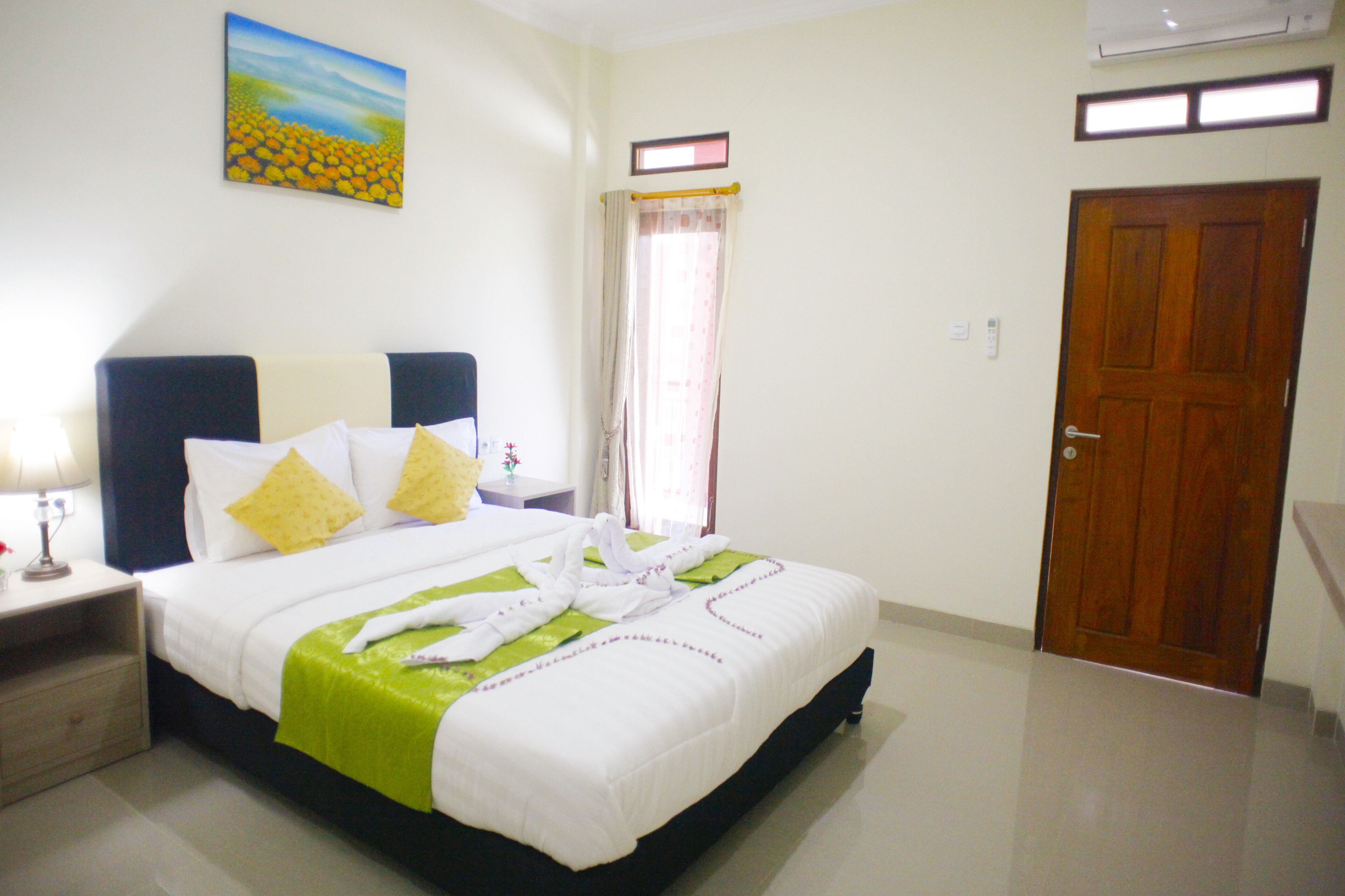 A hotel room with a bed, a nightstand, a lamp, a painting on the wall, a window with curtains, and a door.