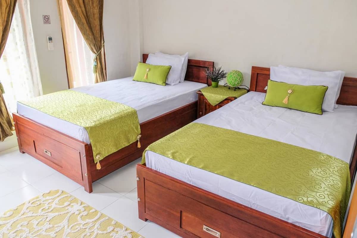 A hotel room with two wooden beds, each with a green bedspread and white linens. There is a small potted plant on one bed and a green decorative pillow on the other.