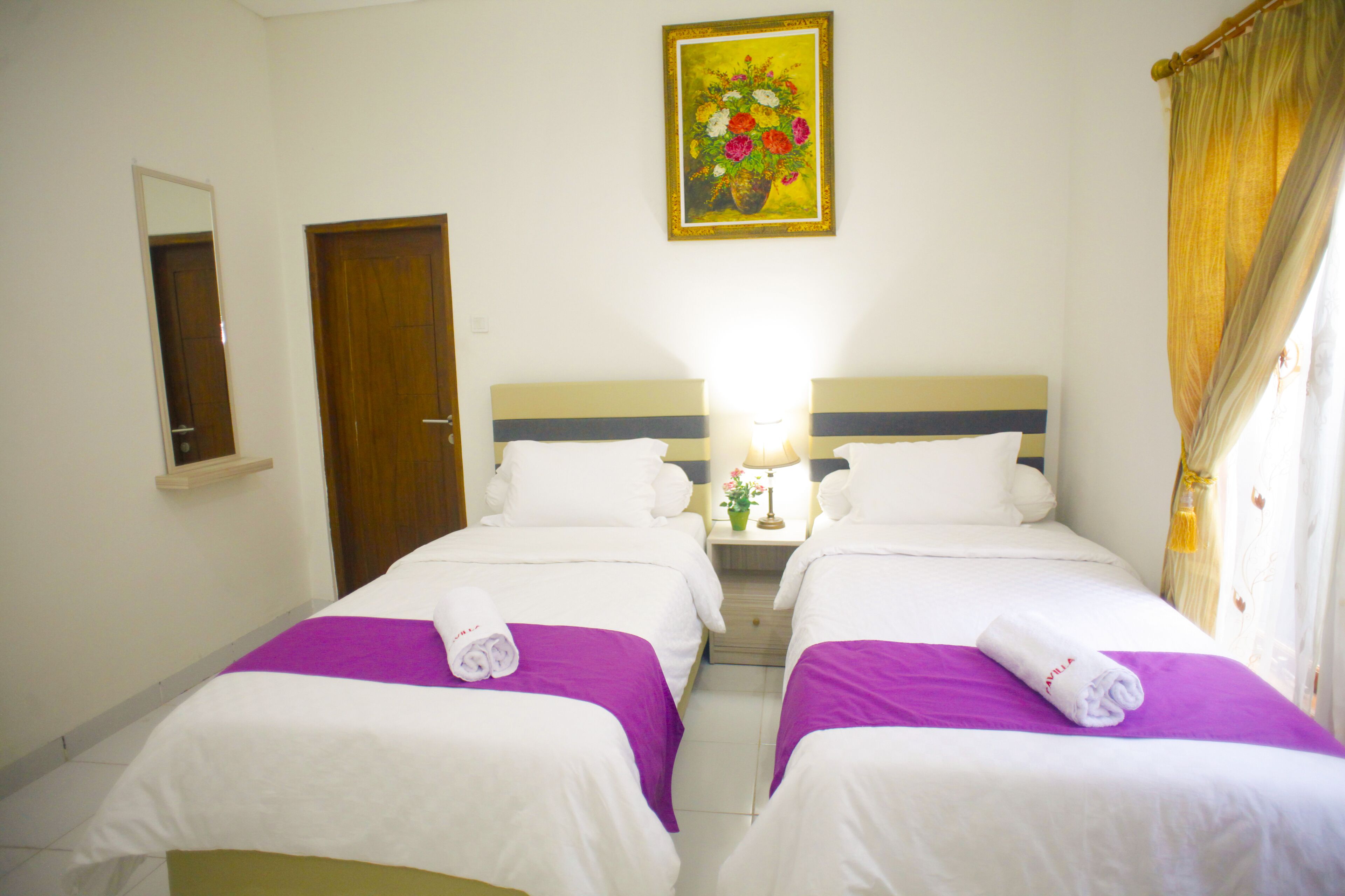 Quarto de hotel com duas camas, mesa de cabeceira, espelho, quadro e janela com cortinas.