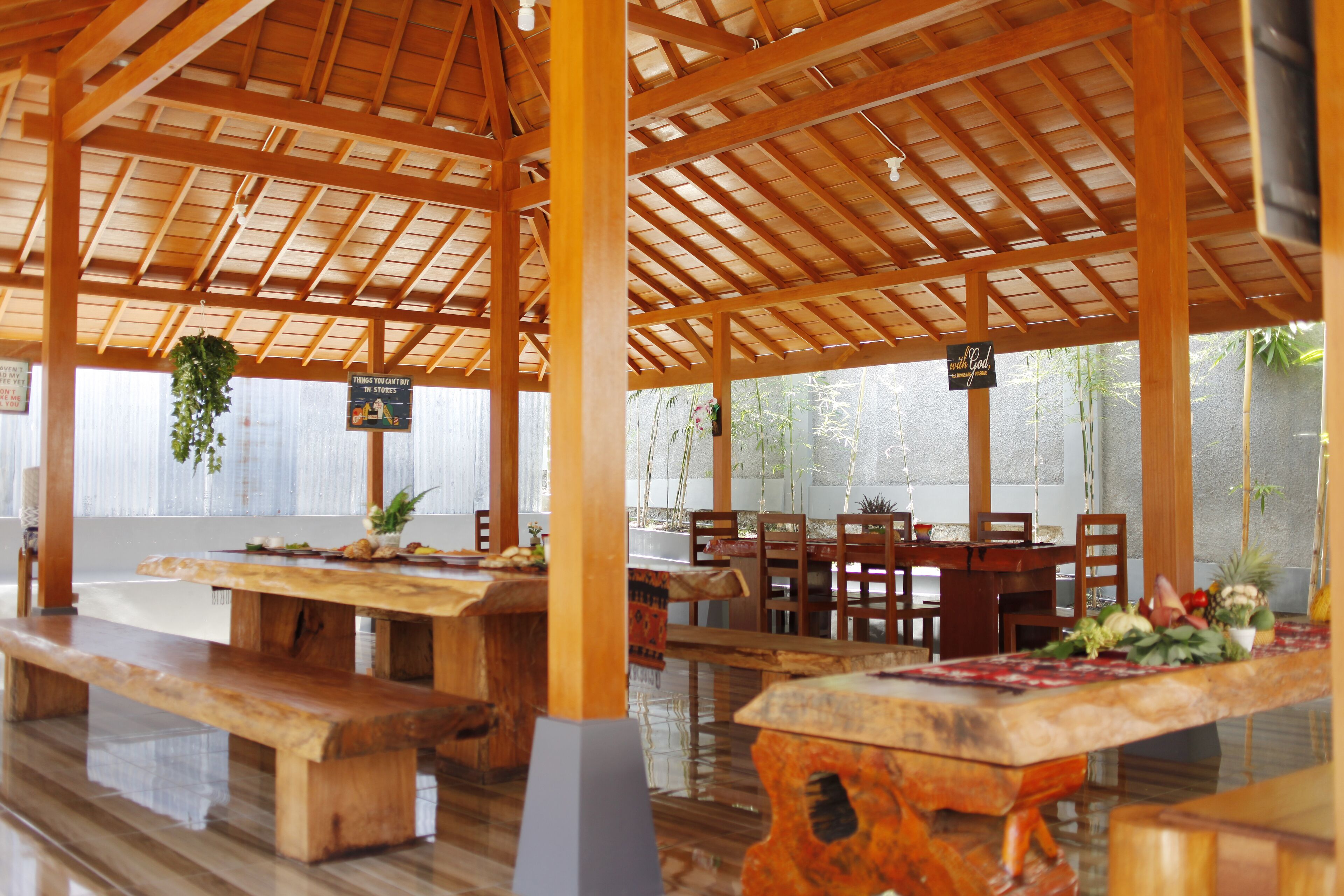 A covered outdoor dining area with wooden tables and benches, a sign indicating a restaurant, and a view of greenery outside.