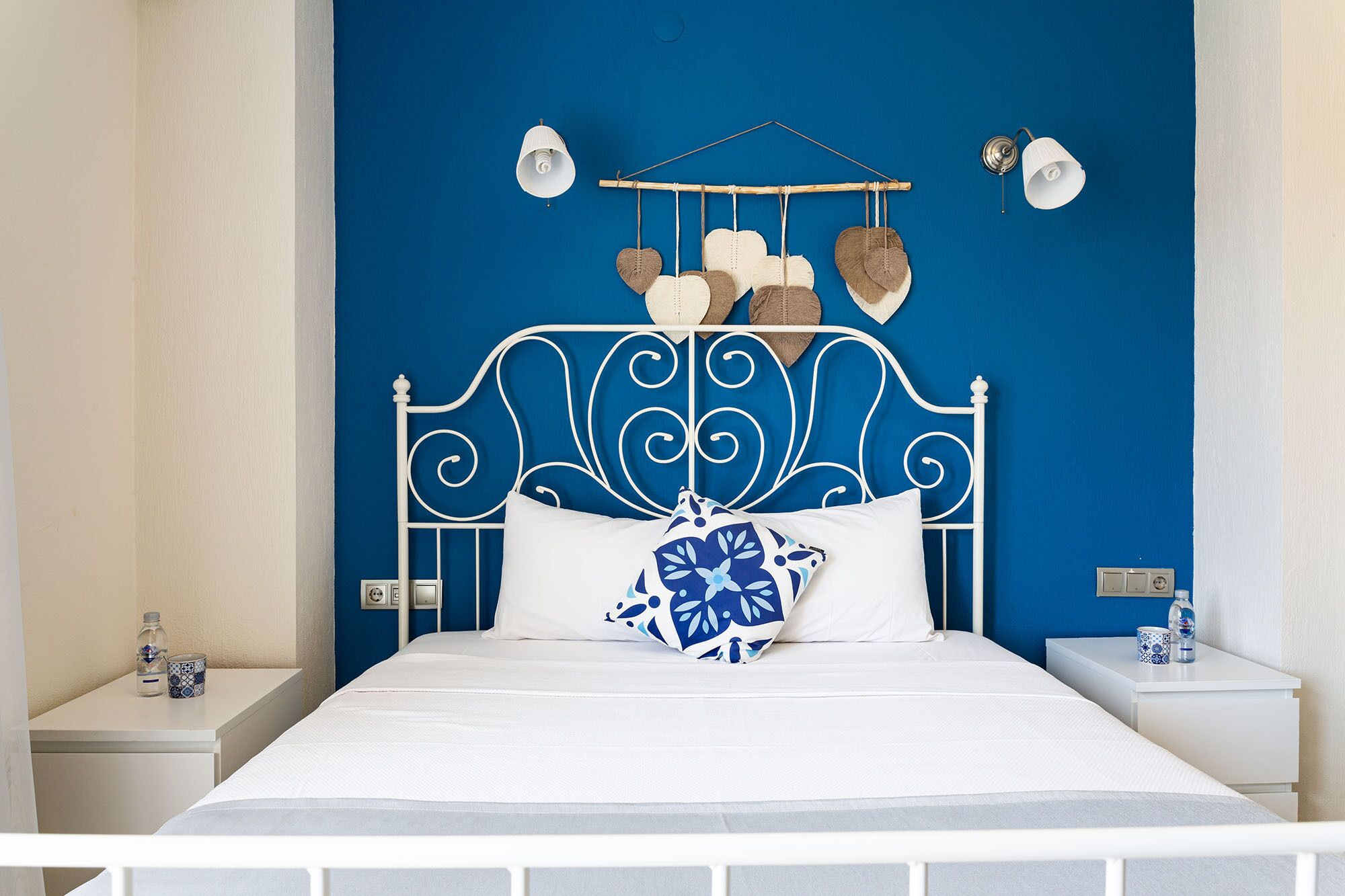 Una cama con estructura metálica blanca y pared azul de fondo.