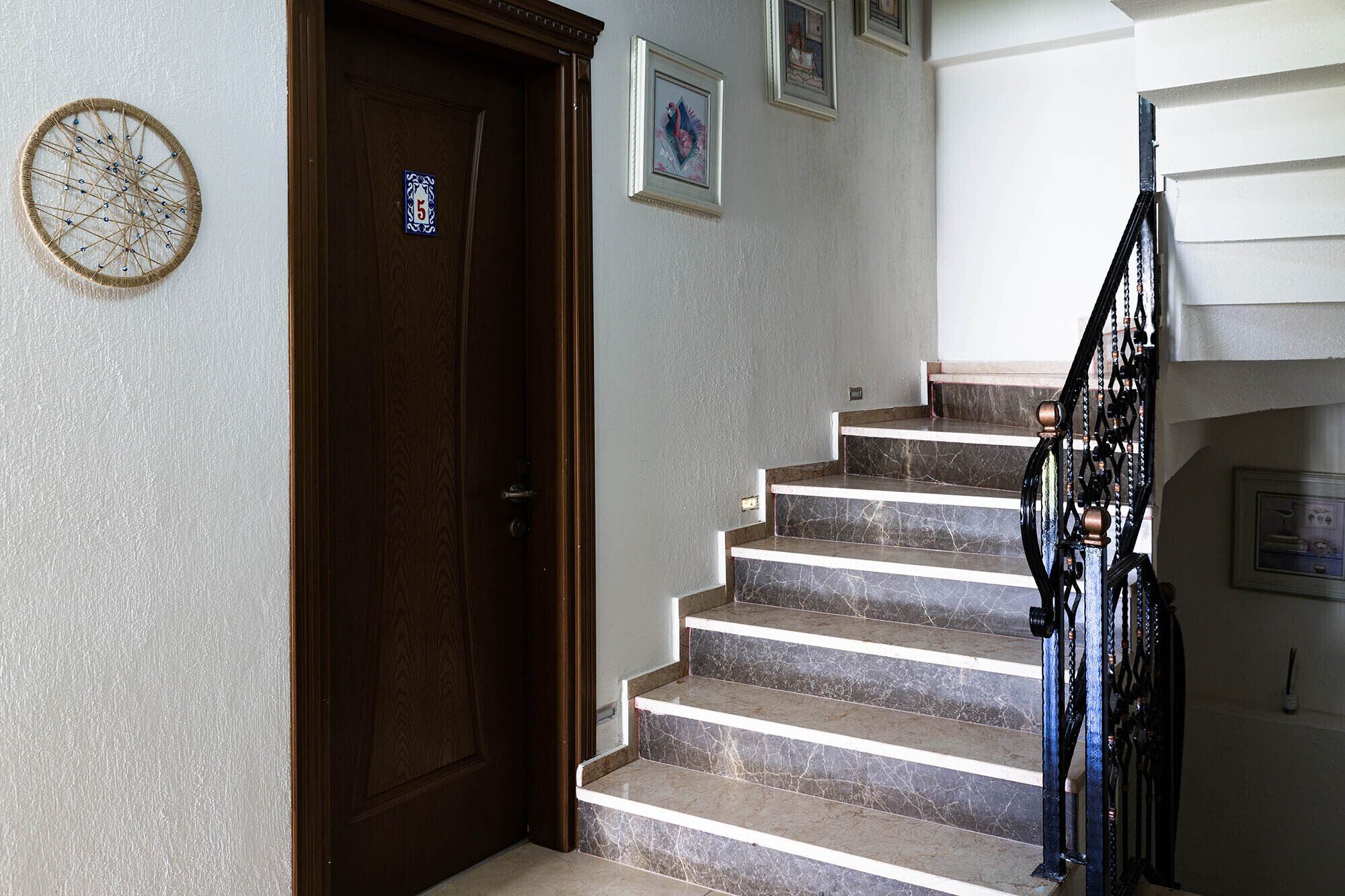 Una escalera con escalones de mármol que lleva a una plataforma, una puerta de madera con una placa de número y obras de arte colgadas en la pared.