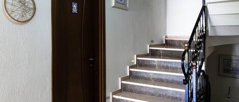 Una escalera con escalones de mármol que lleva a una plataforma, una puerta de madera con una placa de número y obras de arte colgadas en la pared.
