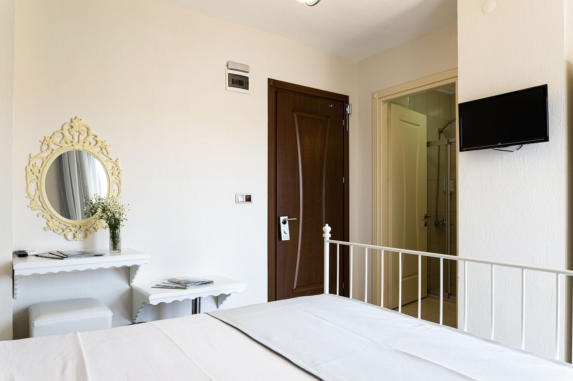 A bedroom with a bed, a bedside table, a mirror, a door, and a TV mounted on the wall.