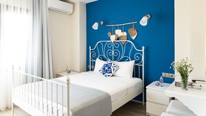 A bedroom with a white bed, a blue accent wall, a white bedside table, and a white nightstand. - Cunda Eren Otel (Ayvalik)