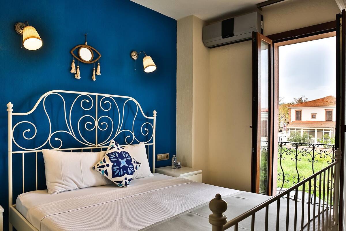 A bedroom with a bed, a nightstand, and a balcony with a railing.