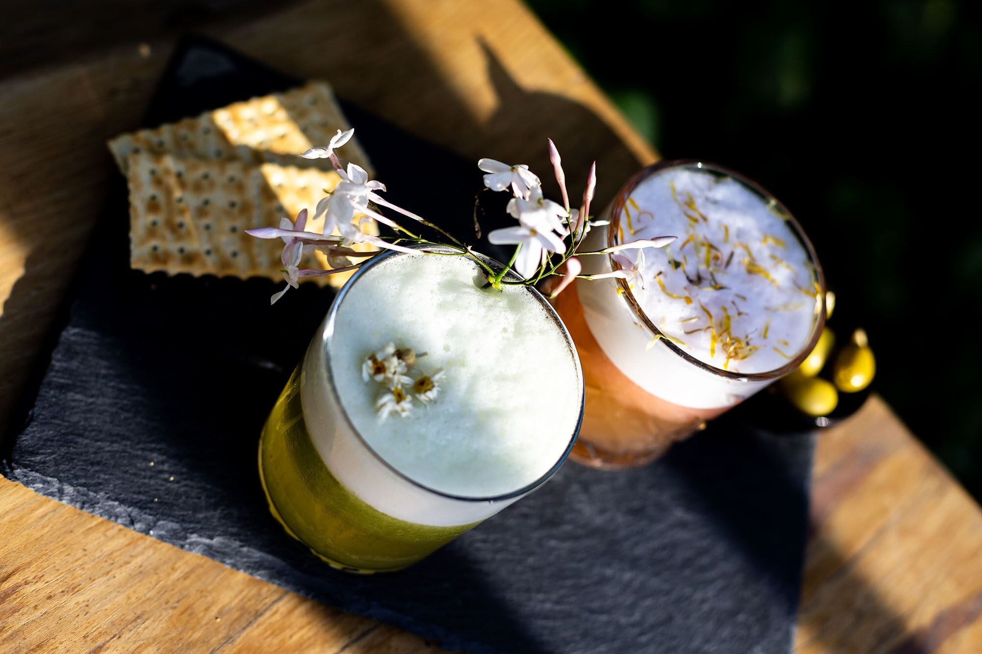 Dos vasos de una bebida blanca con flores, sobre una superficie de madera con un paño oscuro debajo.
