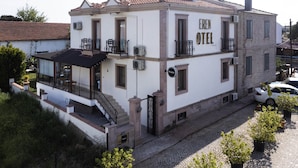 A two-story building with a sign reading "Eren Hotel." It features a balcony with a black railing, a covered outdoor seating area, and a staircase leading to the entrance. - Cunda Eren Otel (Ayvalik)