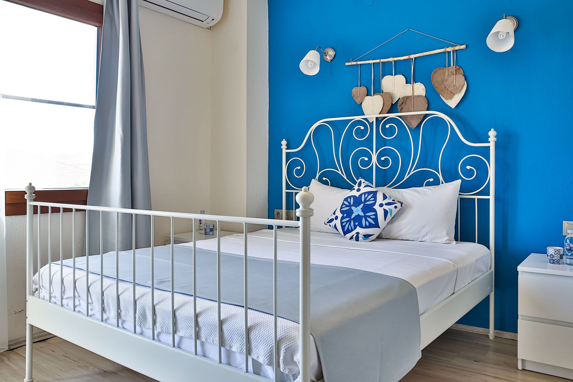 A bedroom with a white metal bed frame, a blue wall, and a white nightstand with a lamp.