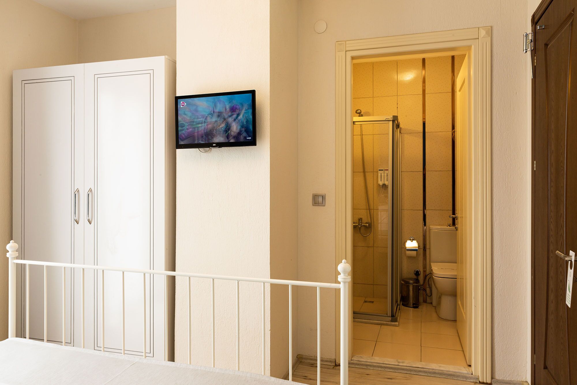 Habitación de hotel con ducha, inodoro y televisor montado en la pared.