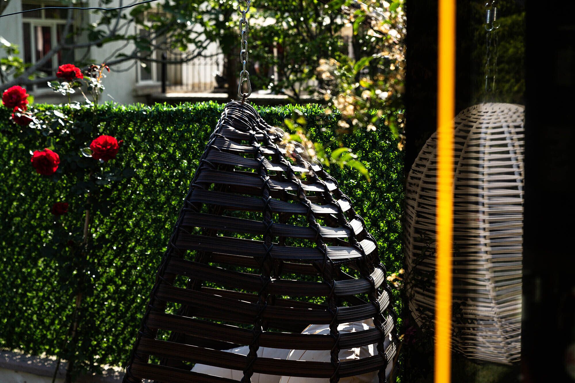 A black metal bench with a geometric design, positioned in front of a neatly trimmed hedge and red flowers.