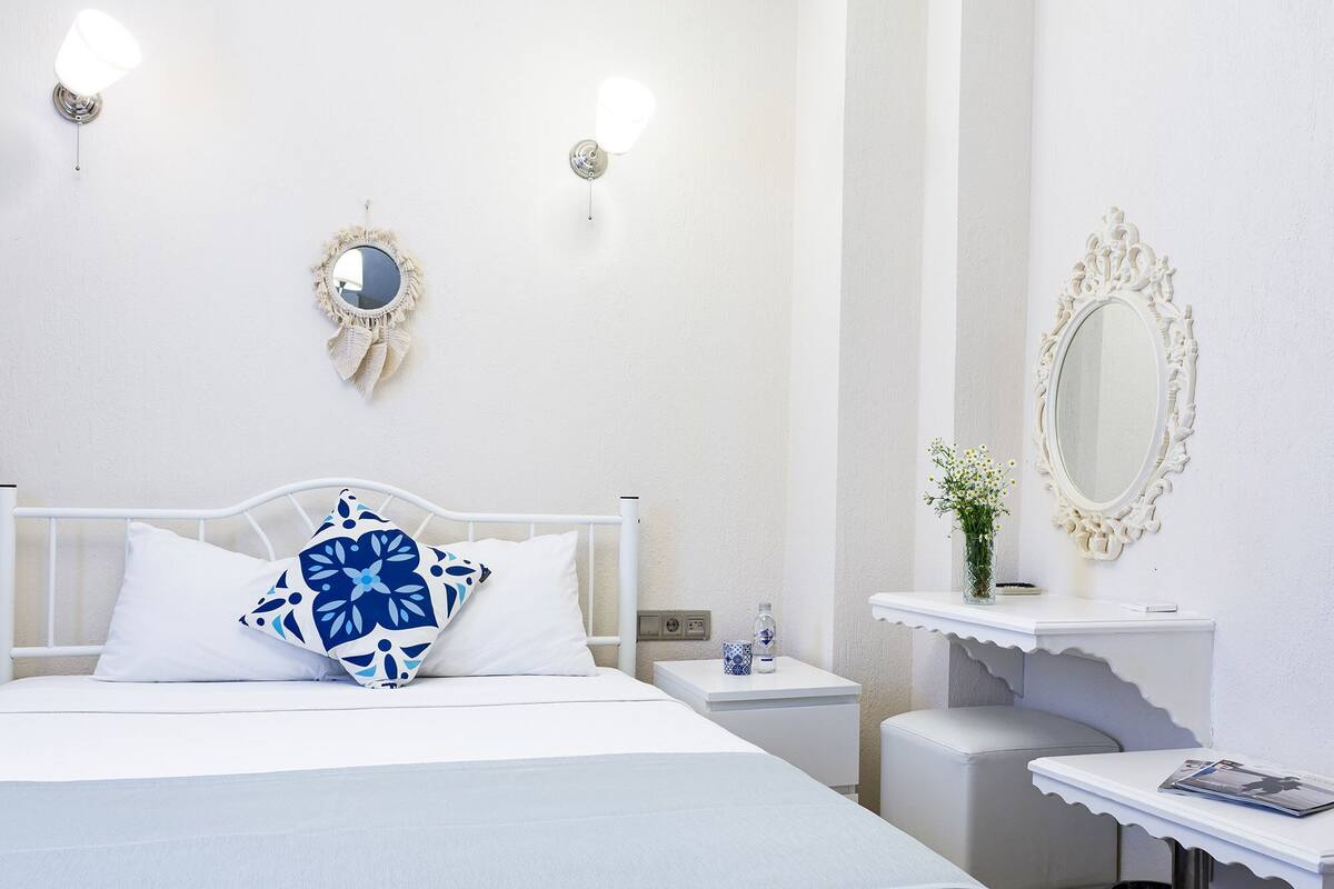 A hotel room with a bed, bedside tables, a vanity with a mirror, and a small stool.