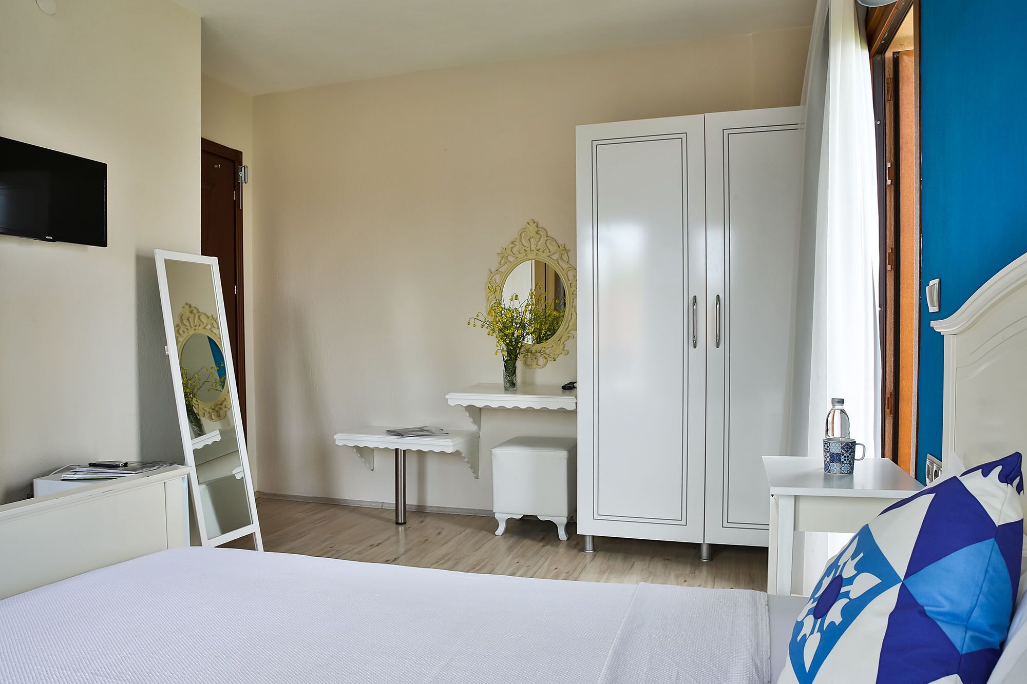 Un dormitorio con cama, armario, escritorio, espejo y ventana con cortinas.