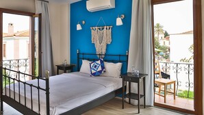 A bedroom with a bed, two bedside tables, a macrame wall hanging, an air conditioning unit, and a balcony with a view of the city. - Cunda Eren Otel (Ayvalik)
