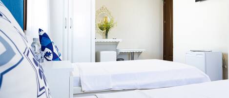A hotel room with two beds, a white wardrobe, a small desk with a mirror, and a television mounted on the wall.