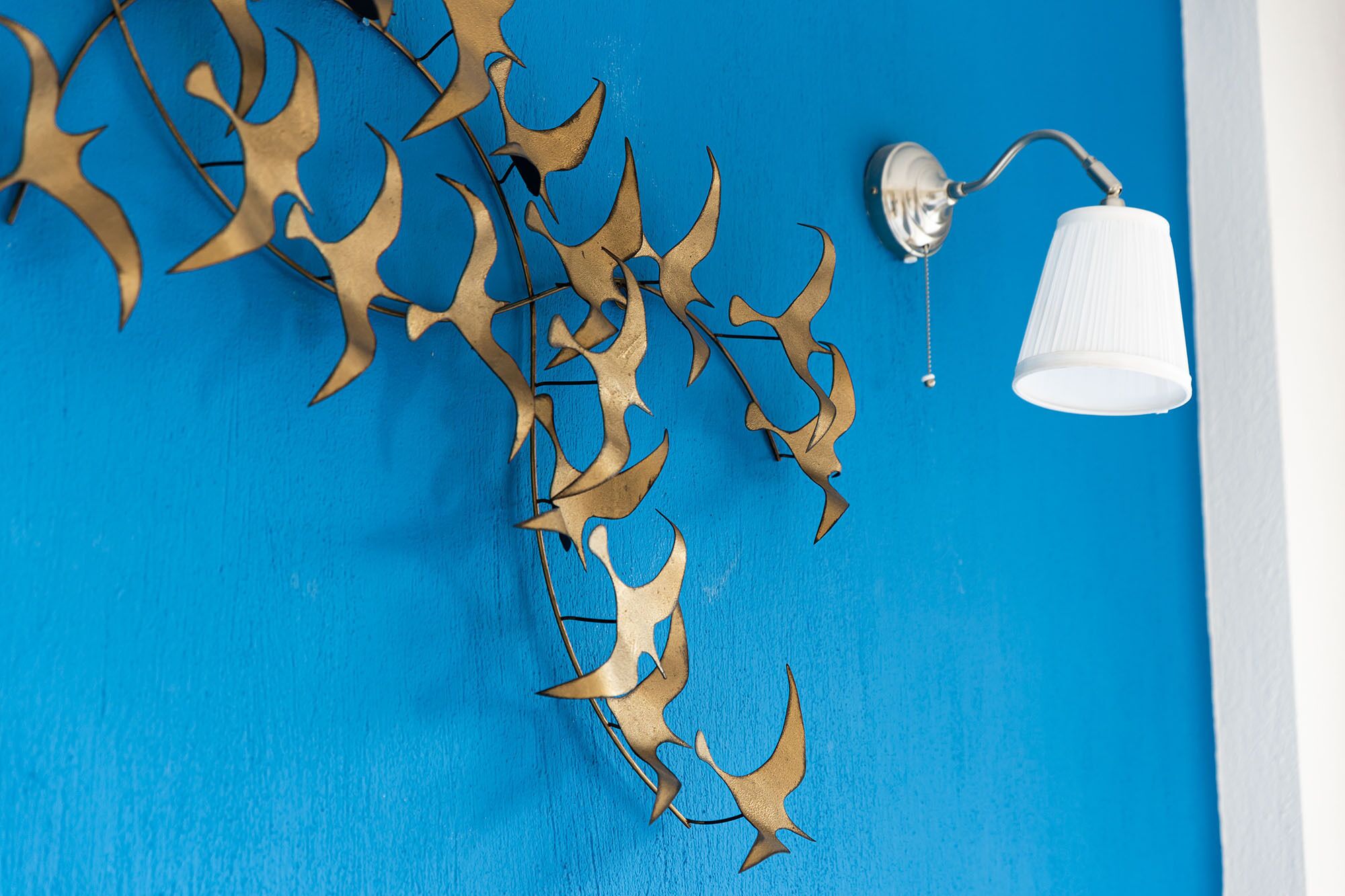 A blue wall with a white lamp and a decorative metal piece.