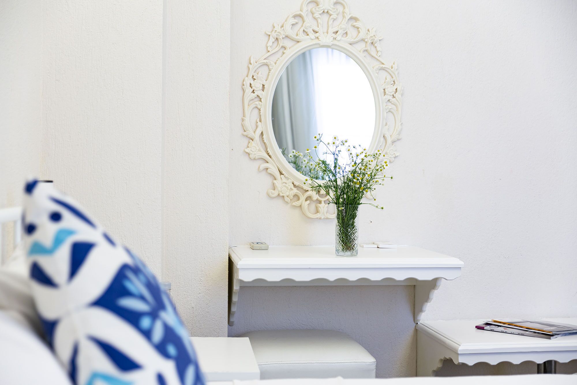 Un baño con tocador blanco, un espejo con marco ornamentado y un florero con flores.