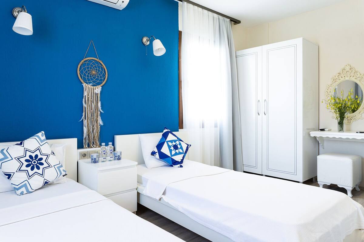 A hotel room with two beds, a wardrobe, a vanity with a mirror, and a dreamcatcher on the wall.