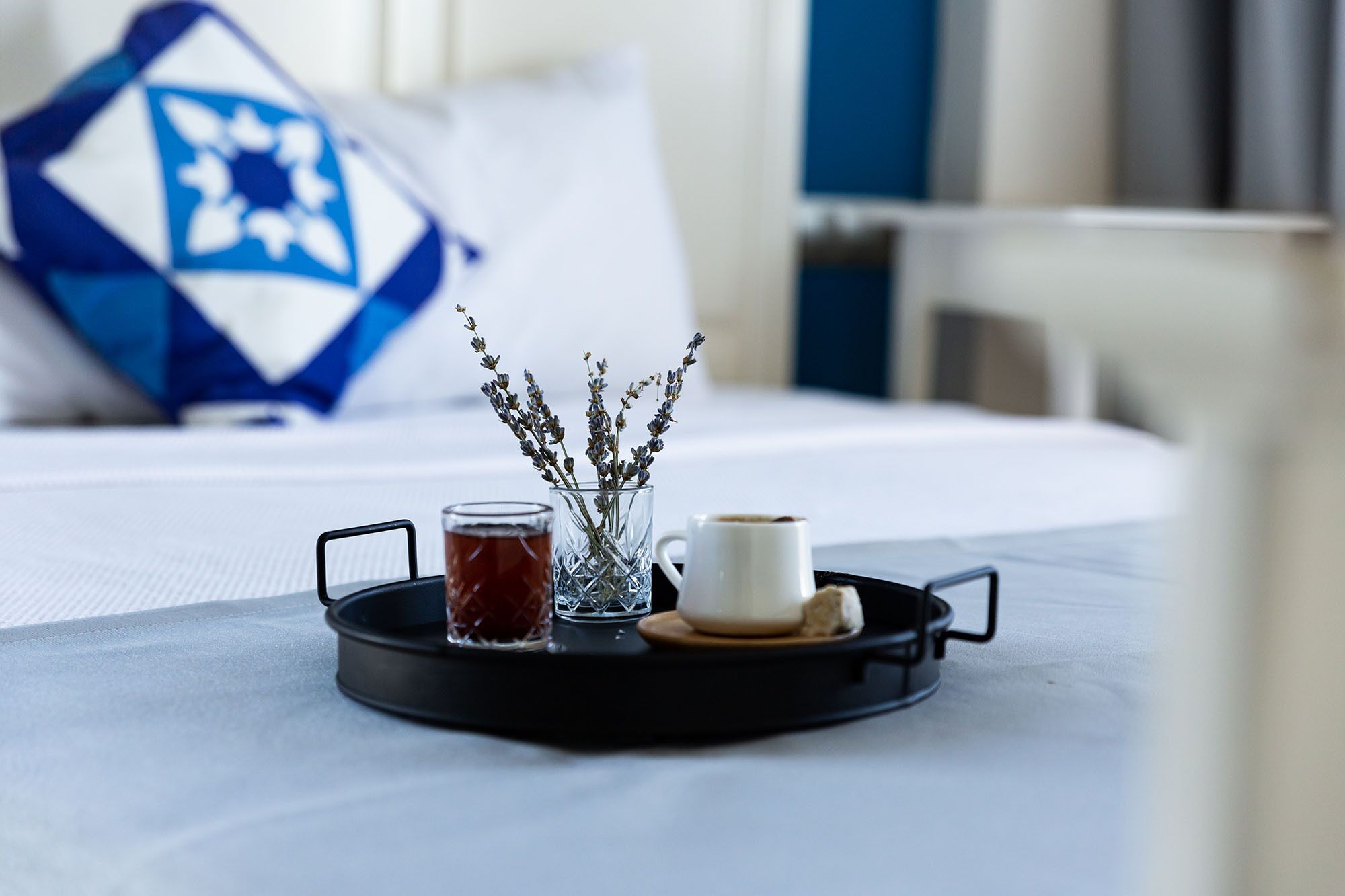 Una bandeja con una taza de té, una taza de café y un florero con lavanda sobre una cama.