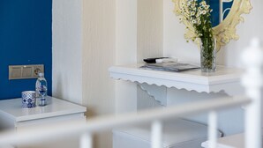 A room with a white vanity, a mirror with ornate detailing, a vase with flowers, a remote control, and a bottle of water on a small table. - Cunda Eren Otel (Ayvalik)