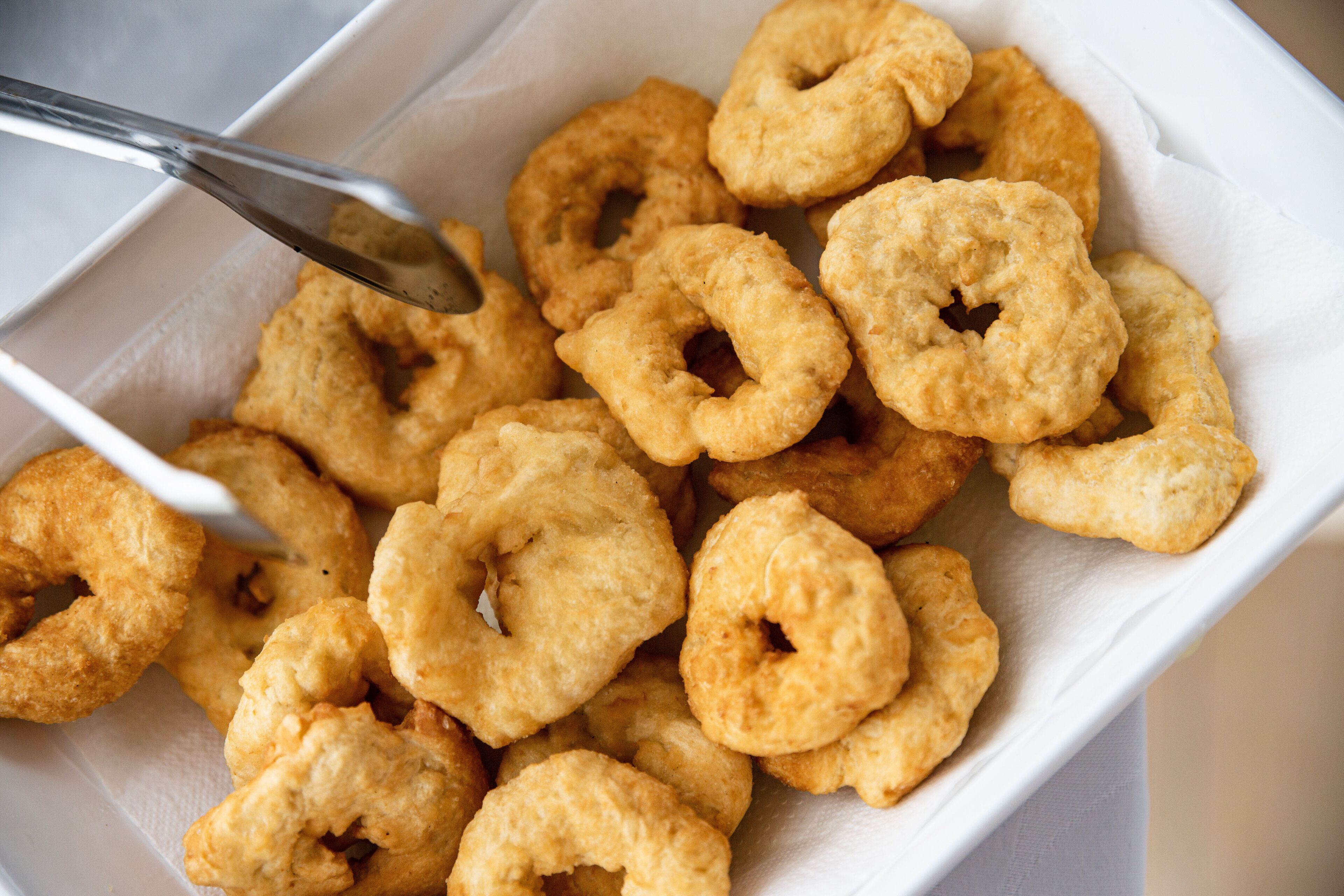 A white paper container filled with golden-brown, ring-shaped fried snacks.